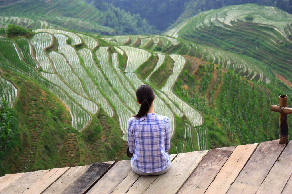 Flicka sitter och tittat ut över risterasserna i Longji, drakens ryggrad i Kina - favoritländer